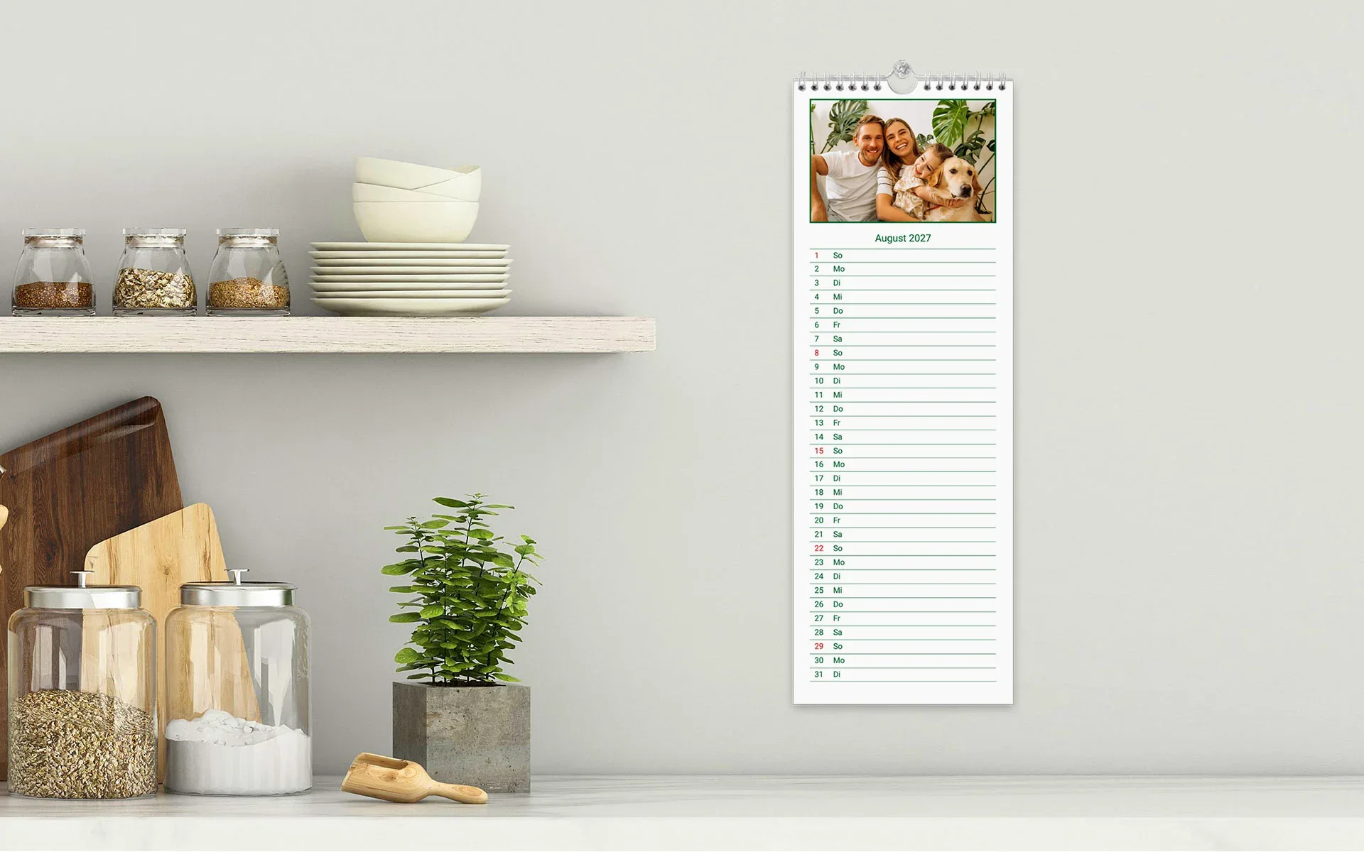 Küchenkalender – aufgehängt Ein aufgehängter Küchenkalender zeigt eine Familie mit Hund in einem grünem Rahmen vor weißem Hintergrund.