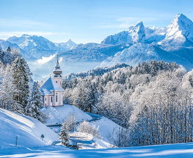 Eine verschneite Landschaft mit einer kleinen Kirche vor majestätischen Bergen.