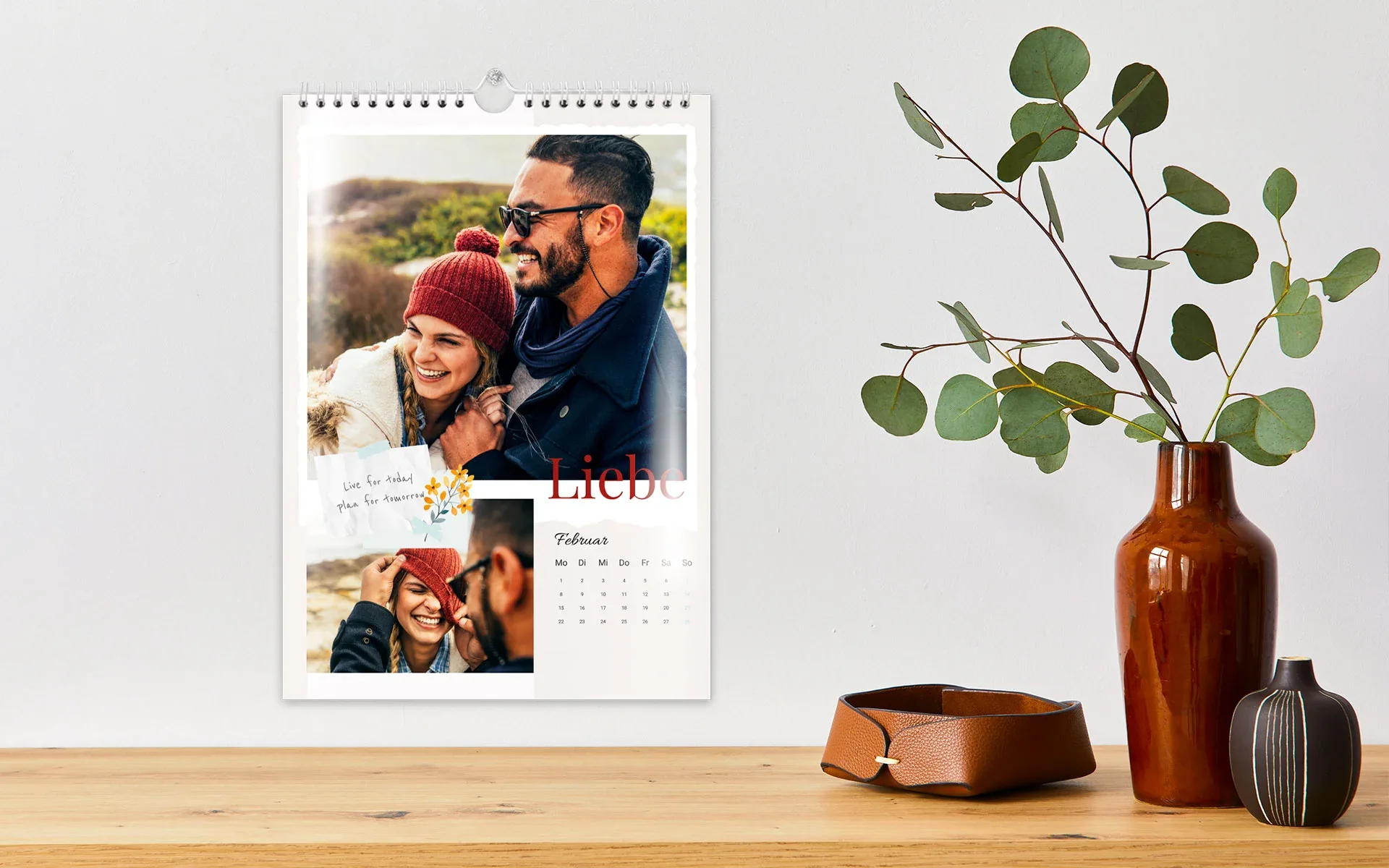 Ein aufgehängter HappyFotokalender ca. A3 hoch mit dem Text Liebe zeigt ein Pärchen und ein Blumen Clipart.