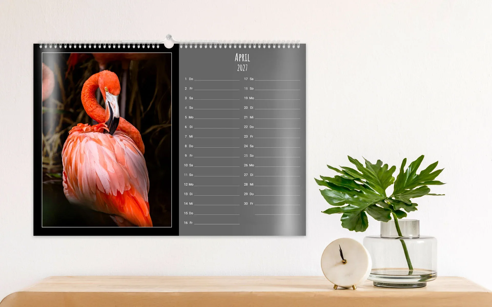 HappyFotokalender ca. A3 quer – aufgehängt Ein aufgehängter HappyFotokalender ca. A3 quer zeigt ein großes Kalendarium, daneben einen Flamingo vor dunklem Hintergrund.