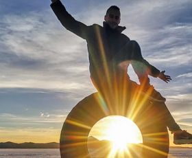 Ein Mann sitzt auf einem Reifen und posiert vor einem Sonnenuntergang, der Strahlen ausstrahlt.