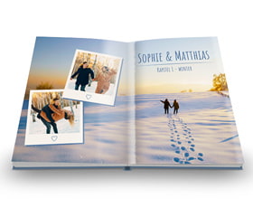 Ein geöffnetes Buch mit Fotos von Sophie und Matthias in einer winterlichen Landschaft. Fußspuren im Schnee sind sichtbar.
