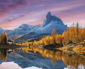 Berglandschaft mit schneebedecktem Gipfel und herbstlichen Bäumen, die sich im ruhigen Wasser spiegeln.