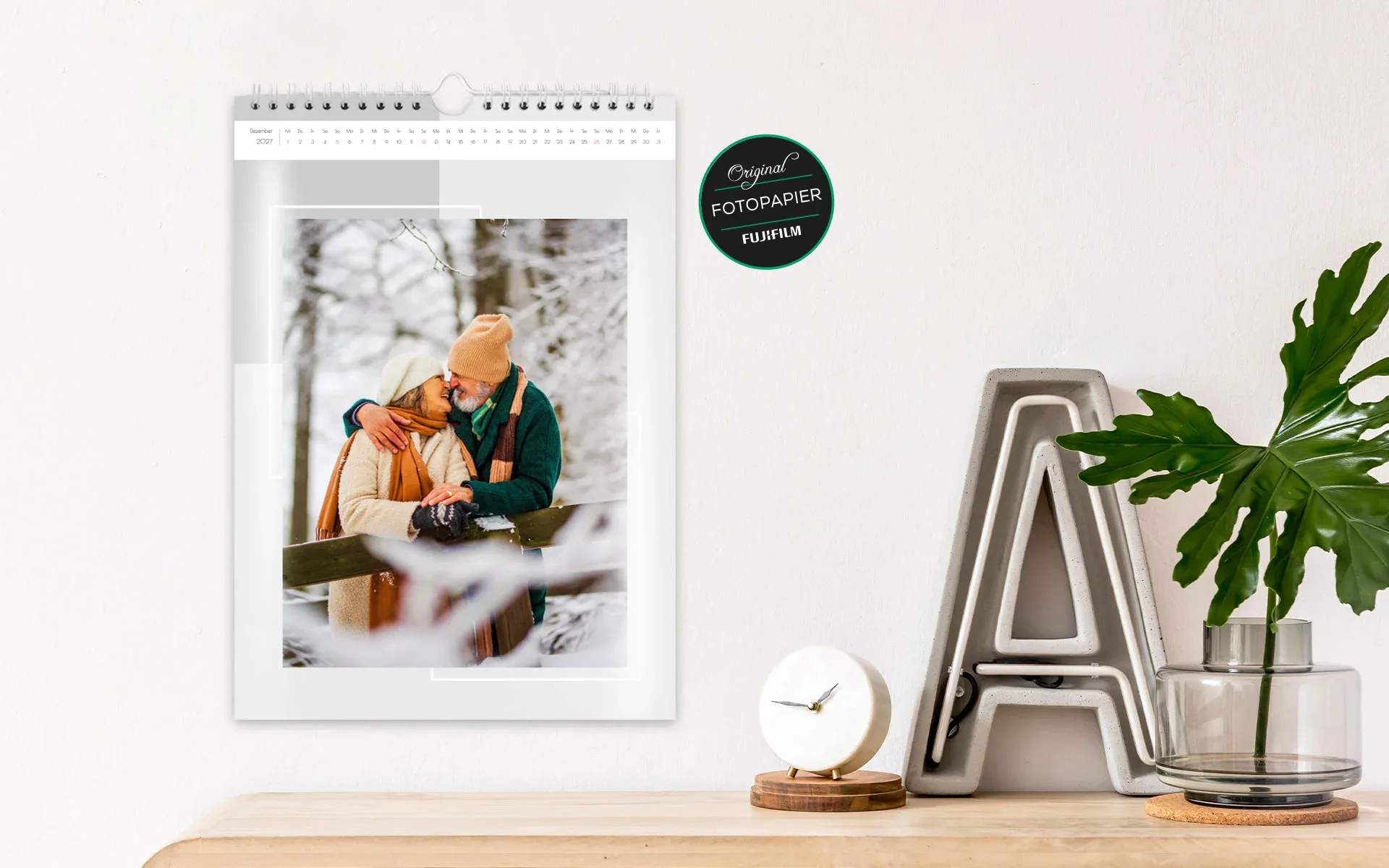 Ein aufgehängter HappyFotokalender ca. A3 hoch zeigt ein älteres Pärchen im verschneiten Wald vor grauem Hintergrund.