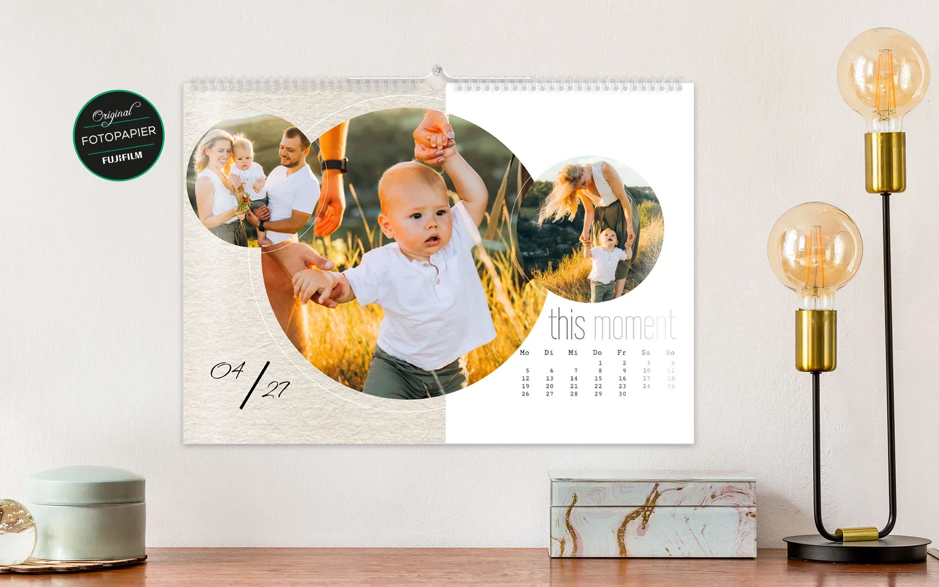 Ein aufgehängter HappyFotokalender ca. A4 quer mit dem Text This Moment zeigt 3 Fotos einer Familie in kreisförmigen Rahmen.